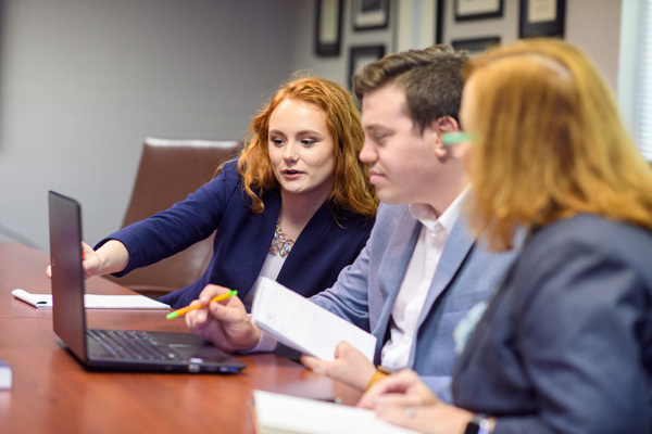 three people looking at a laptop one is point at the screen