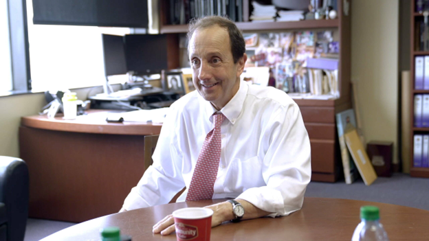 man in white shirt sits at desk in office