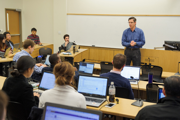 Professor teaching in front of classroom all students have laptops open. 