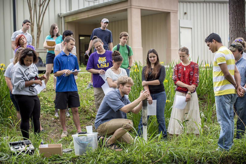 a group of people take notes and observe a sediment core