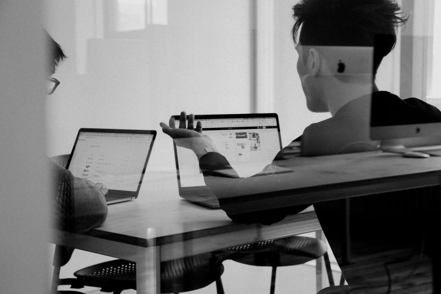 two people talk in front of two laptop computers